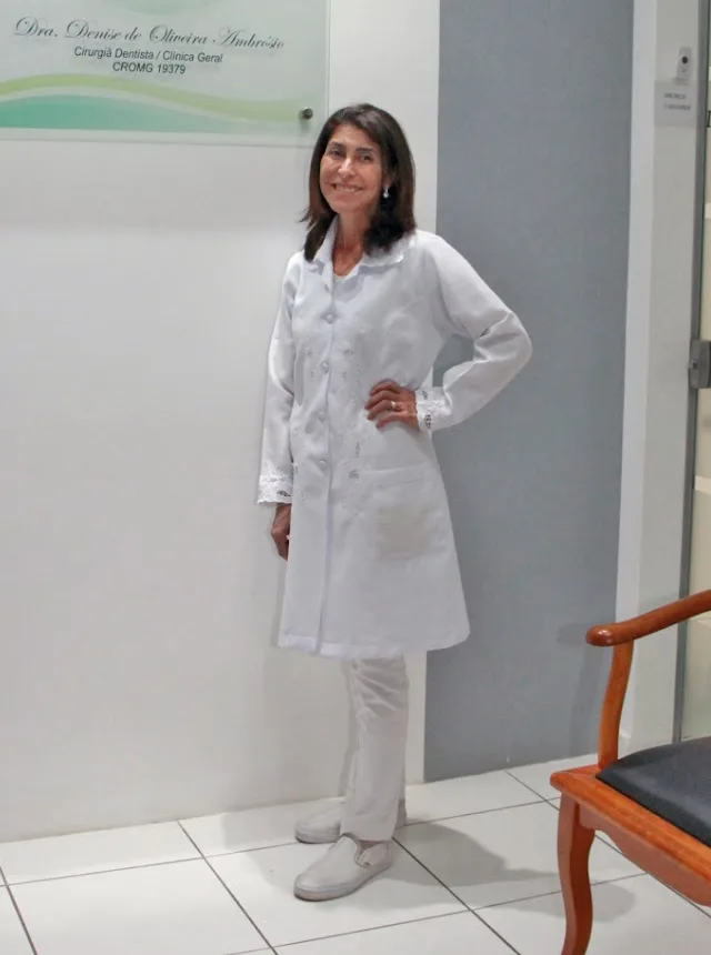 Dra. Denise de Oliveira Ambrósio, de jaleco branco, na recepção do consultório