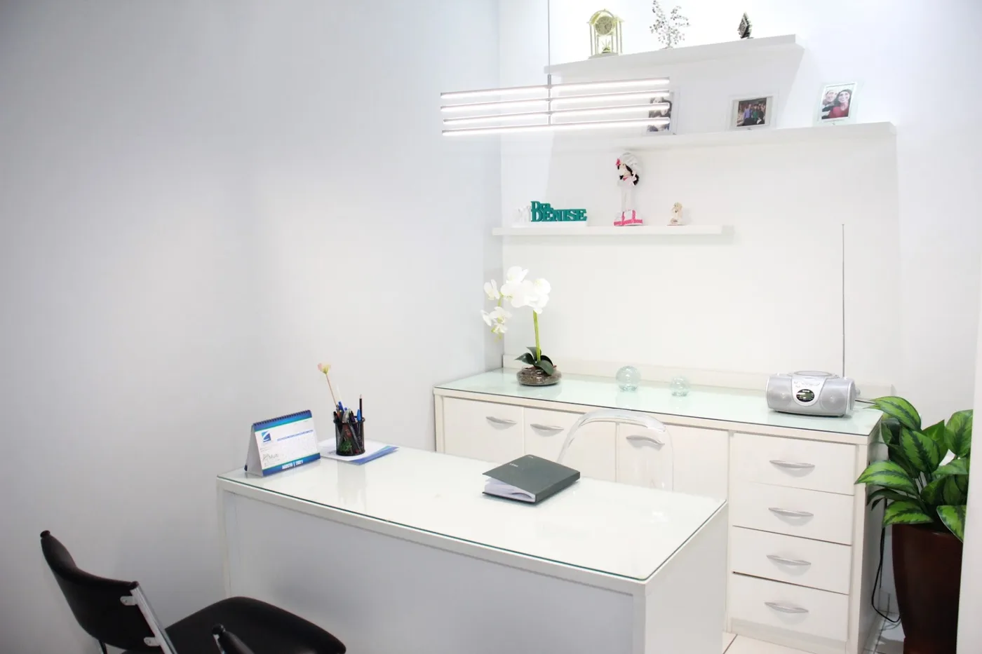 Sala do consultório, branca, com mesa, armários e uma orquídea